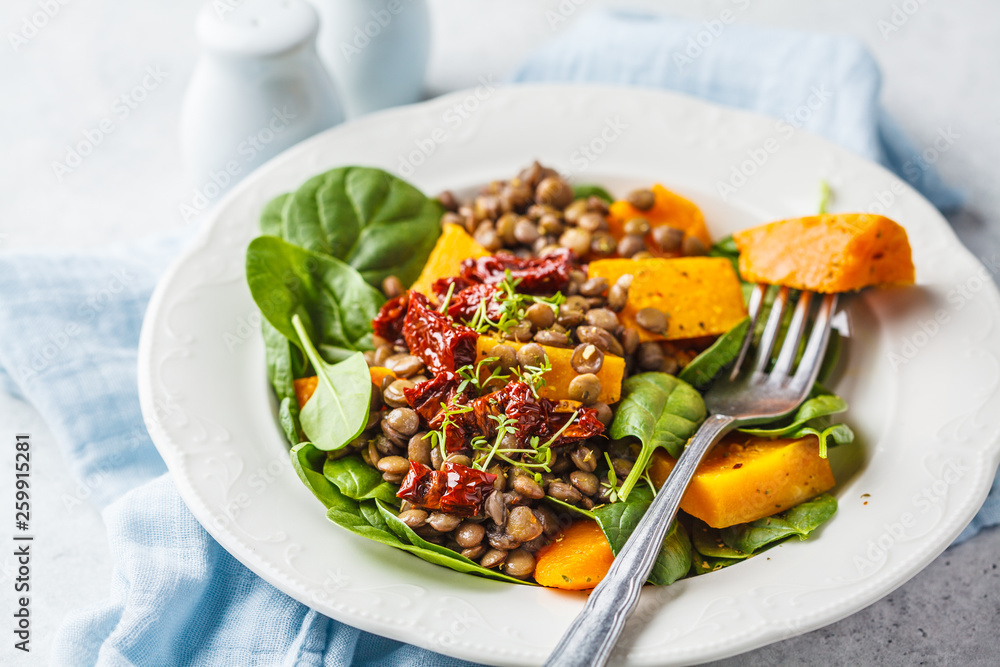 Vegan salad with lentils, pumpkin and dried tomatoes in white plate.