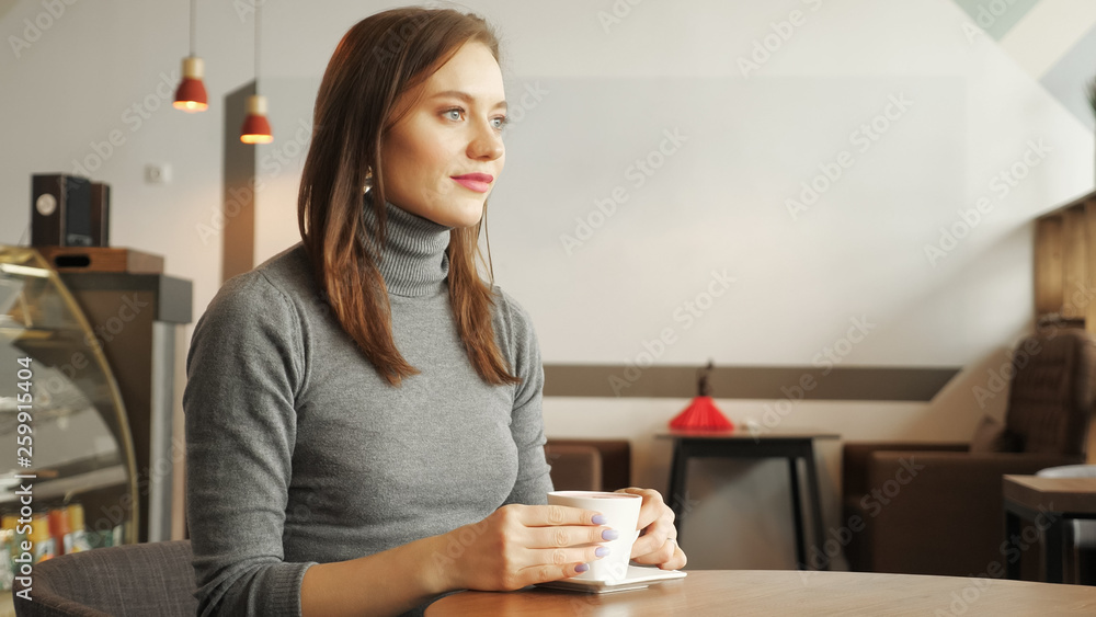 Young women is drinking a cup of coffee sitting in cafe in the city. Side view. Young women is drinking a cup of coffee sitting in cafe in the city. Side view.