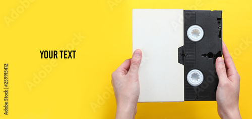 Принти на полотні Woman hands holding videocassette in cover, videotape on a yellow background with copy space for your text