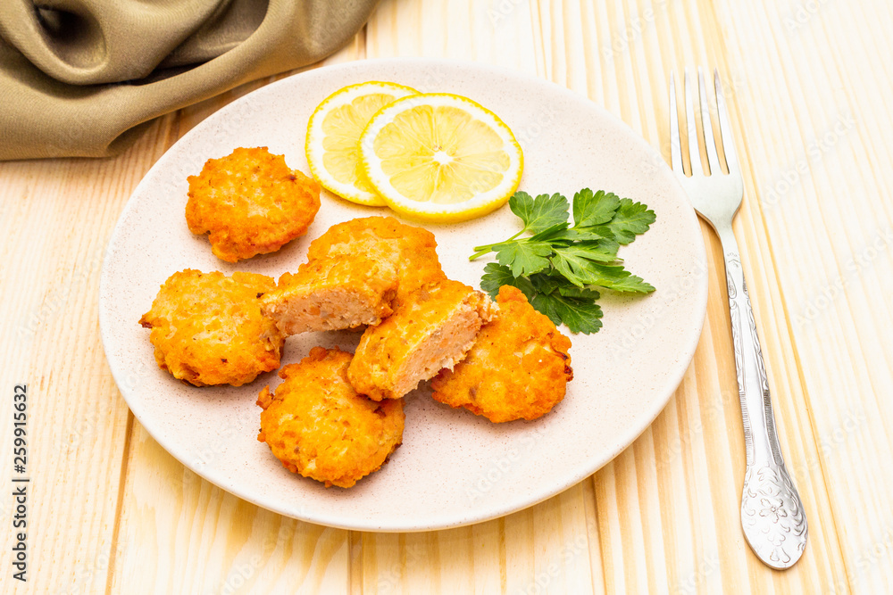 Homemade red fish cakes with lemon and parsley in ceramic plate. With fabric drapery and fork on wooden background, close up. Homemade red fish cakes with lemon and parsley in ceramic plate. With fabric drapery and fork on wooden background, close up.