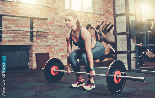 Fitness girl in sportswear doing deadlift exercise with barbell at gym.
