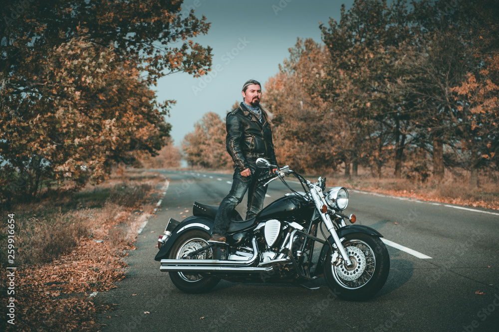 Stylish biker posing with motorcycle on the road.