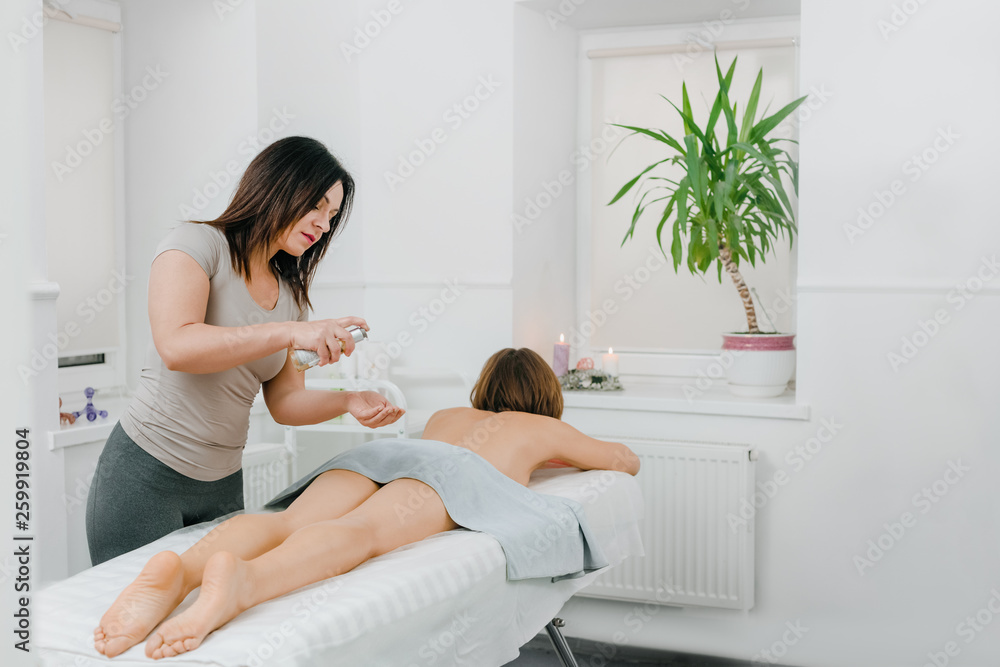 Female professional masseur applying oil on back of her client Female professional masseur applying oil on back of her client
