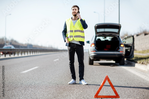 Fotografi Man in vest calling road assistance standing near the broken car on the highway
