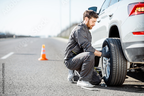 Handsome road assistance worker in uniform changing car wheel on the highway photo