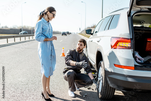 фотографія Road assistance worker helping young woman to change a car wheel on the highway
