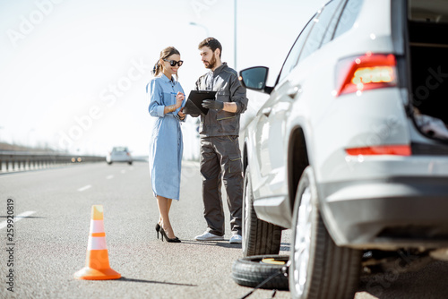 Tableau sur toile Road assistance worker signing some documents with woman near the broken car on