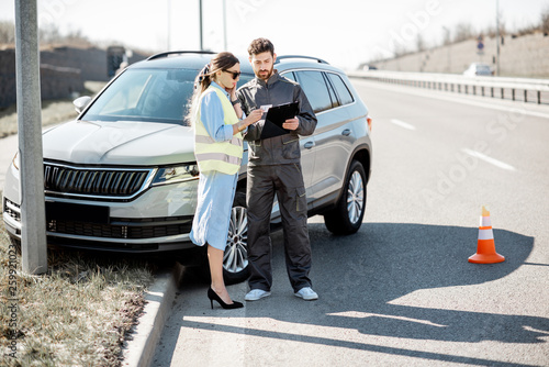 Woman with road assistance worker signing some documents standing near the car in road accident on the highway