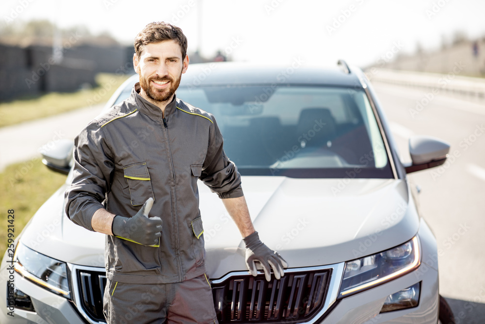 Portrait of a handsome road assistance worker in uniform standing near the car on the roadside Portrait of a handsome road assistance worker in uniform standing near the car on the roadside