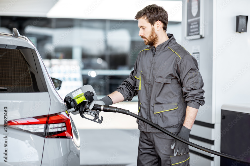 Gas station worker in workwear refueling luxury car with gasoline holding filling gun at the station