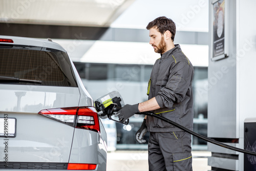 Foto Gas station worker in workwear refueling luxury car with gasoline holding fillin