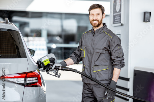 Portrait of a gas station worker in workwear refueling luxury car with gasoline at the station