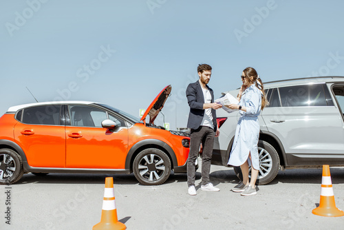 Fotografie Man and woman arguing, standing together on the road with their cars on the back