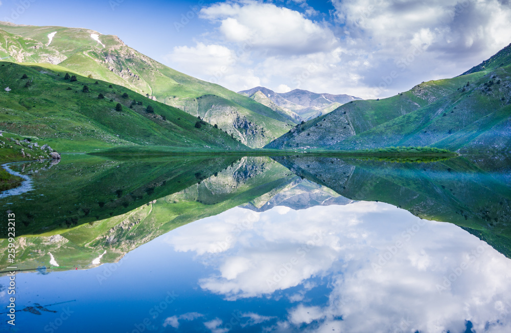 Mountain lake Susyngen, Kazakhstan. Reflection of clouds, green coasts and the blue sky in a surface of the water. 