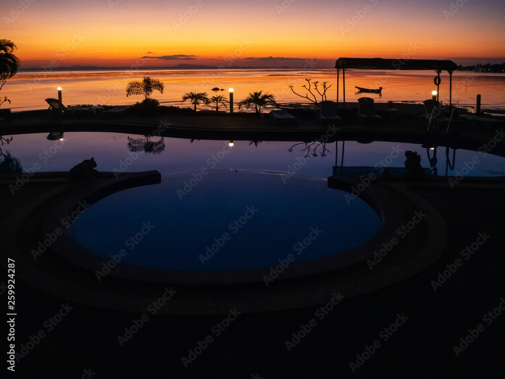 Sunset with a boat and palm trees reflected in the pool