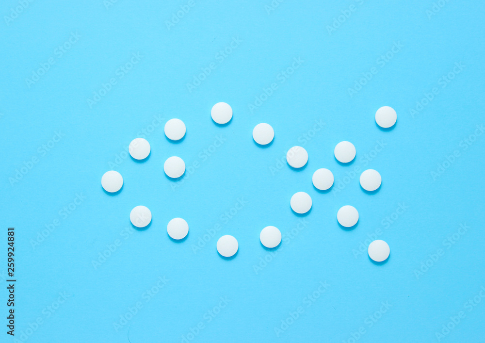 Form of fish laid out of white pills on blue background. Medical minimalistic concept, top view