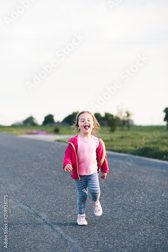 Little adorable girl having fun running on road, sticking her tongue out