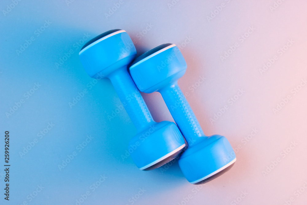 Minimalism sport concept. Two blue plastic dumbbells, blue orange holographic light. Top view Minimalism sport concept. Two blue plastic dumbbells, blue orange holographic light. Top view