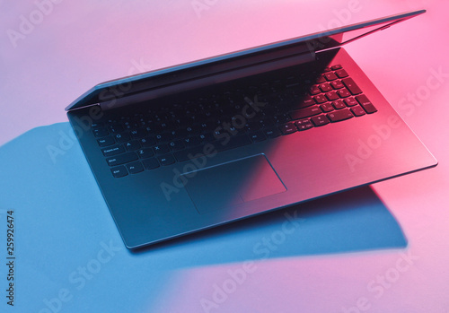 Modern laptop with vibrant gradient pink  blue holographic color lights. Minimal office surrealism concept. photo