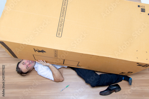 Billede på lærred The unhappy man lying under a big box