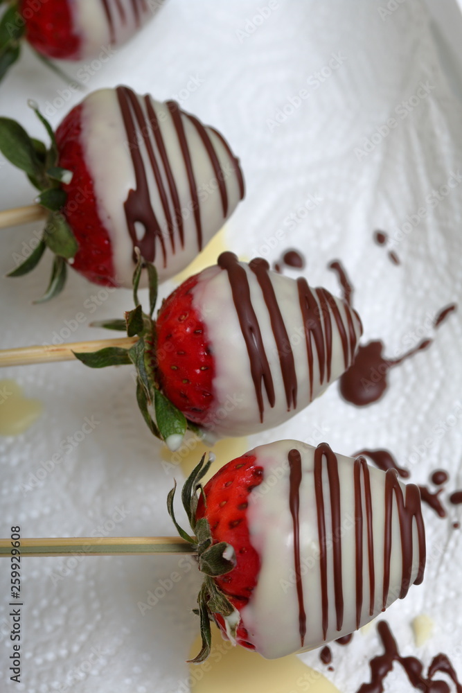 Strawberries glazed in black and white chocolate dries on a plate. On the work surface visible drops of chocolate. Cooking strawberries glazed in chocolate. Strawberries glazed in black and white chocolate dries on a plate. On the work surface visible drops of chocolate. Cooking strawberries glazed in chocolate.