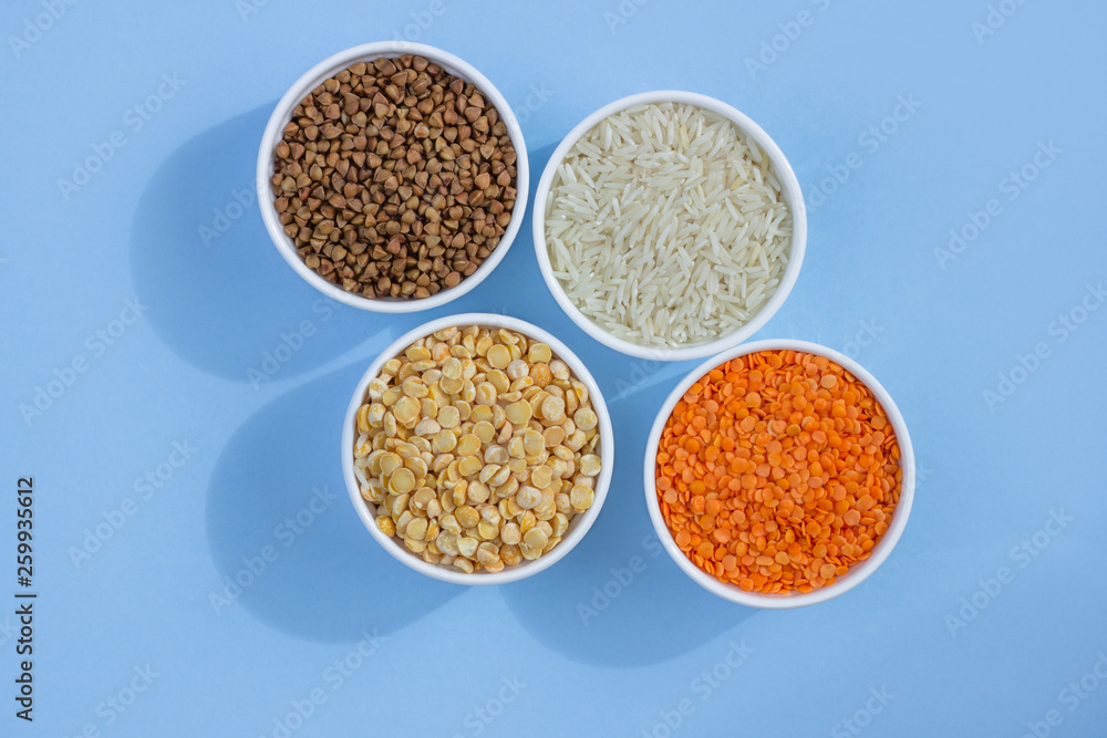 Assorted different cereals on a blue background. Buckwheat, lentils, rice, peas in plates top view, copy space Assorted different cereals on a blue background. Buckwheat, lentils, rice, peas in plates top view, copy space
