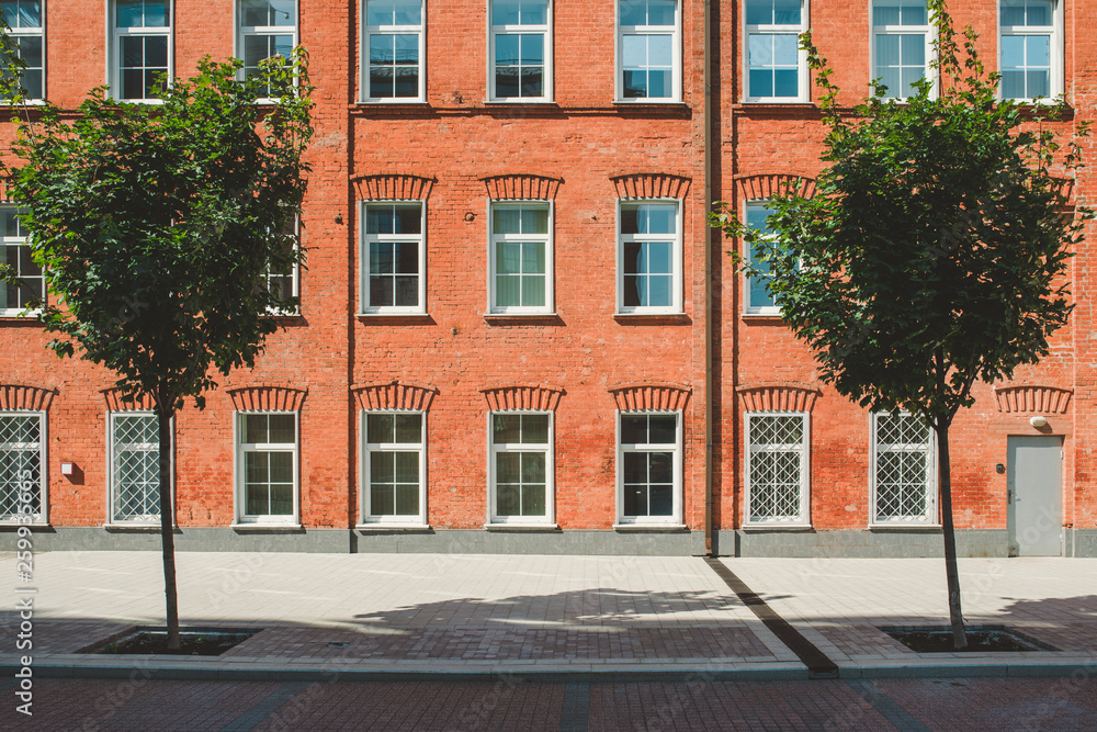 Office building in loft style. Large Windows. Red brick wall. Green bushes on the middle. Flat fasade composition