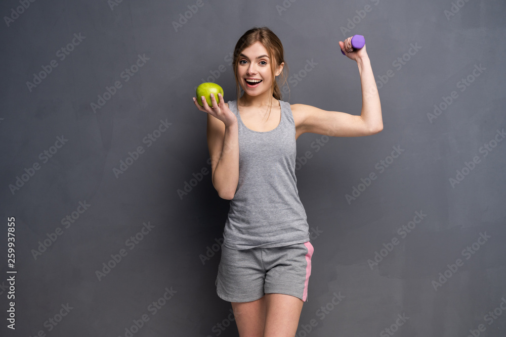 Sporty fit woman holding dumbbells weights in one and apple fruit in another hand. Fitness and healthy dieting concept. Sporty fit woman holding dumbbells weights in one and apple fruit in another hand. Fitness and healthy dieting concept.