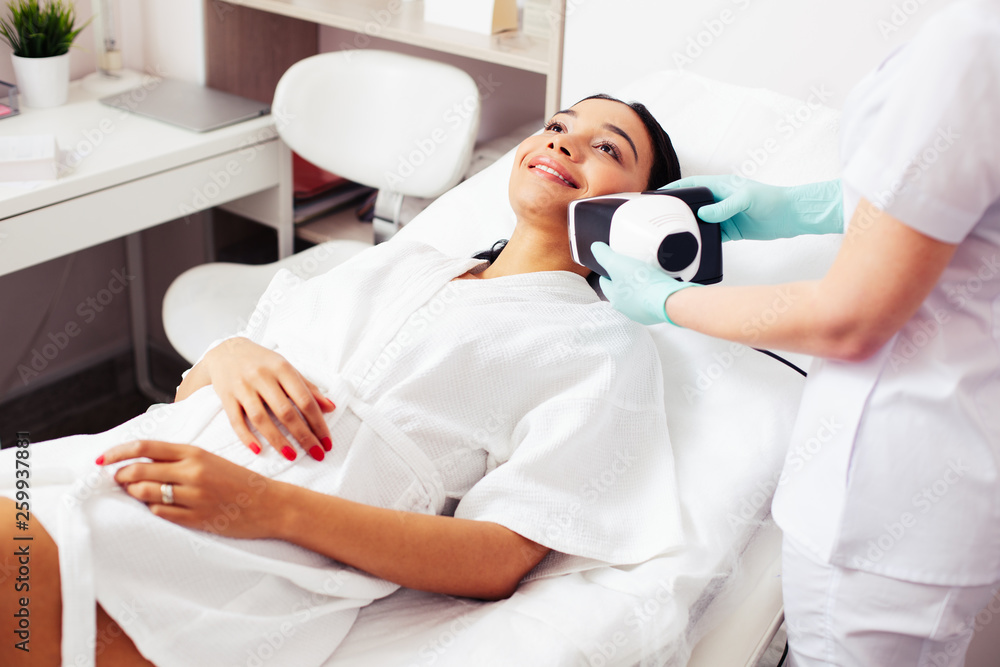 Happy woman in bathrobe undergoing skin analysis Happy woman in bathrobe undergoing skin analysis