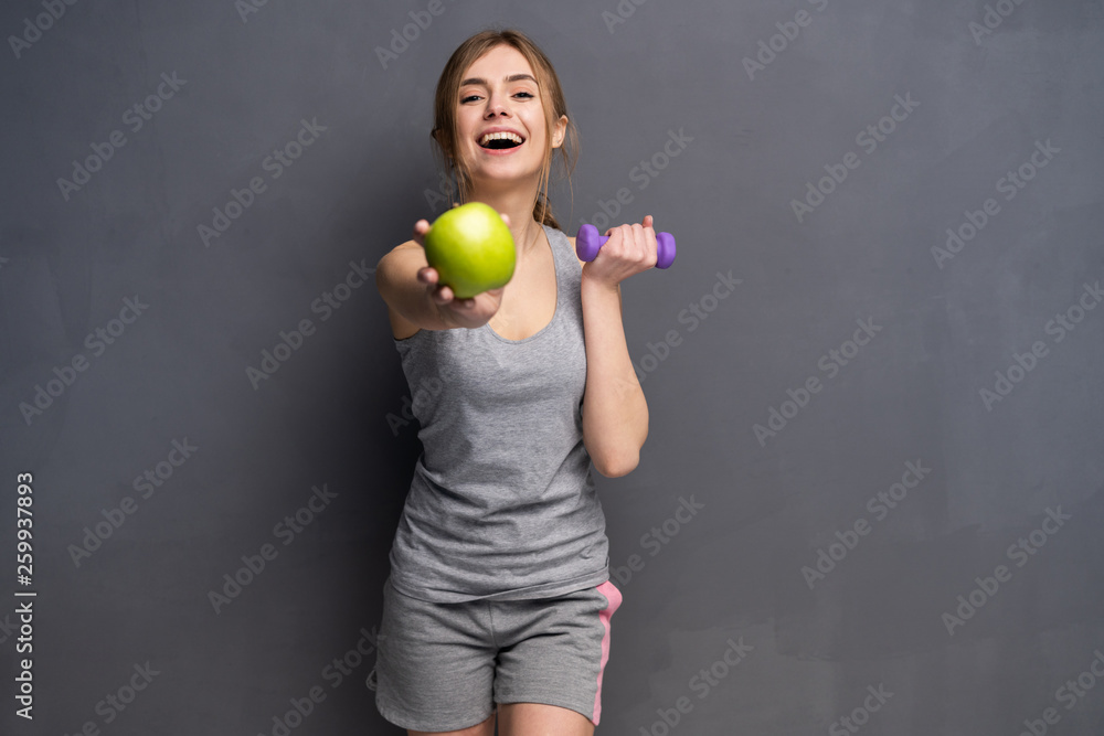 Sporty fit woman holding dumbbells weights in one and apple fruit in another hand. Fitness and healthy dieting concept. Sporty fit woman holding dumbbells weights in one and apple fruit in another hand. Fitness and healthy dieting concept.