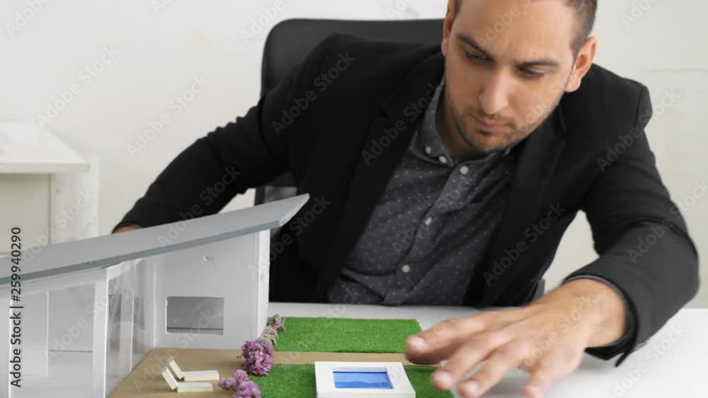Businessman fixes the architecture of a house model with swimming pool and roof Businessman fixes the architecture of a house model with swimming pool and roof