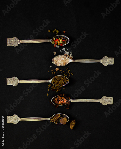 Kitchen concept: spices on spoons, top view, black background, selective focus © Monika