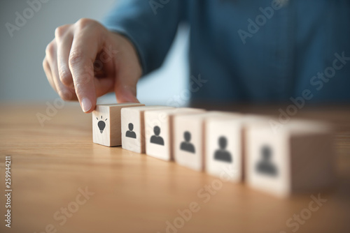 Closeup hand choosing wood cube with idea symbol in people icon.