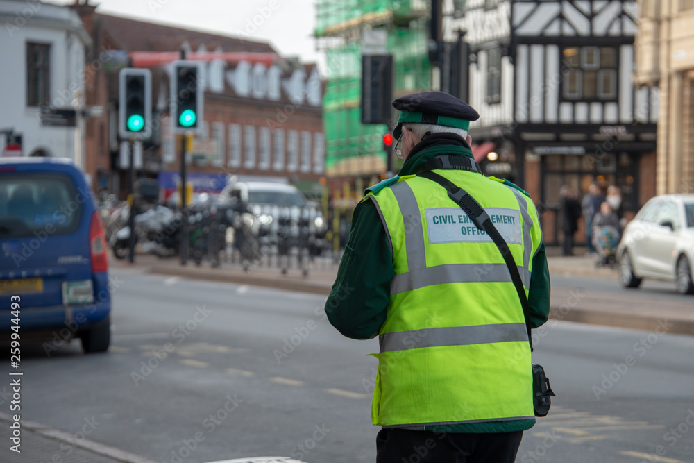 Fototapeta premium civil enforcement officer or traffic warden walks up the street whilst writing a parking ticket in the UK