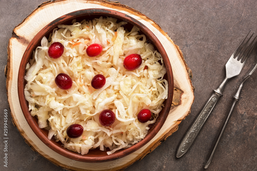 A bowl of sauerkraut with cranberries on a wooden stump, rustic brown background. Top view, flat lay. A bowl of sauerkraut with cranberries on a wooden stump, rustic brown background. Top view, flat lay.