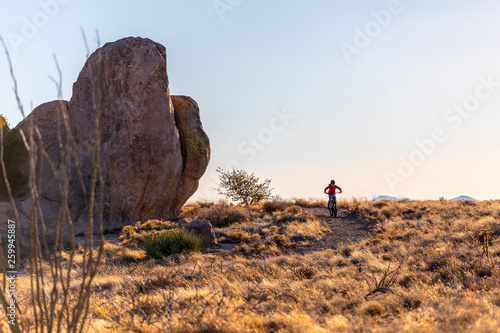 A boy mountain biking around a desert trail with giant boulders