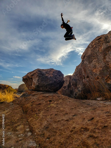 A boy jumps off a huge boulder in the desert