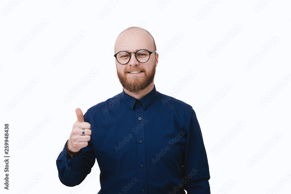 Portrait of a smiling man in glasses showing thumb up over white wall background
