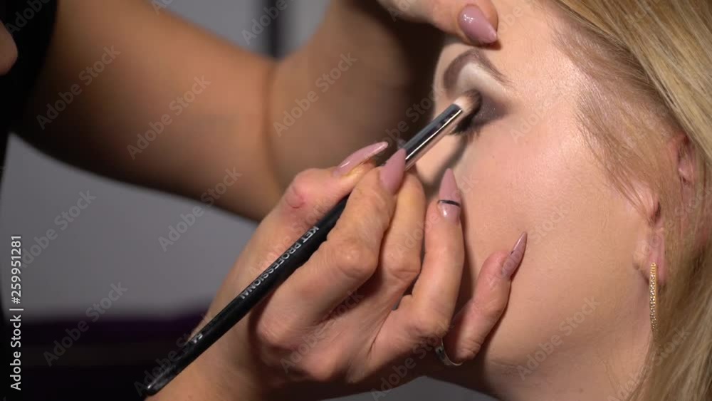 Beauty saloon. Young beautiful girl model is sitting in the chair. Makeup artist makes girl makeup. Makeup artist applies shadows on the eyelids of the model. Beauty saloon. Young beautiful girl model is sitting in the chair. Makeup artist makes girl makeup. Makeup artist applies shadows on the eyelids of the model.