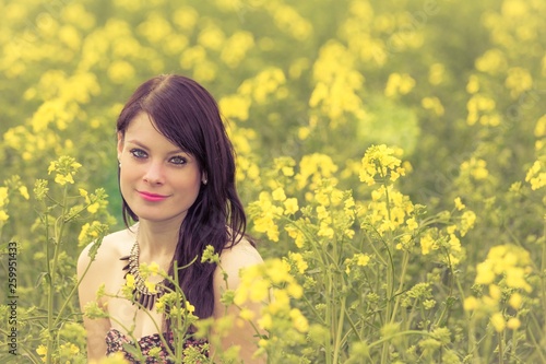 Smiling summer love woman sitting down in rapeseed field happy. Attractive young beauty girl enjoying the warm sunny sun in nature takes time feeling sustainability contemplation and youth wellbeing