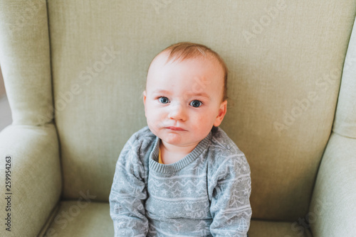 Cute little toddler boy sitting on big armchair