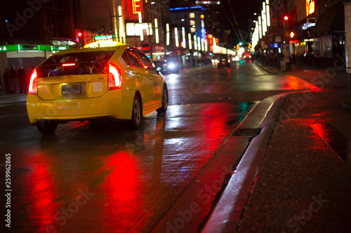 Yellow taxi car driving  rain night city wet asphalt red reflections copy space