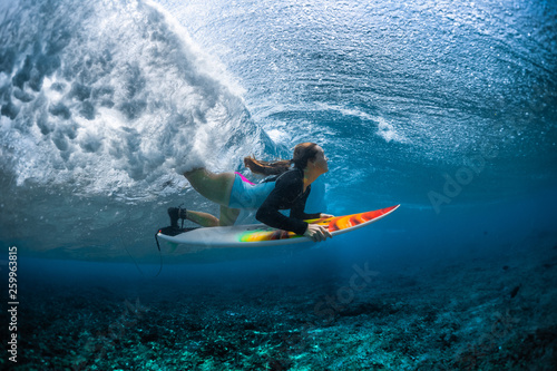 Underwater shot of the young woman surfer diving under the wave with her surfboard