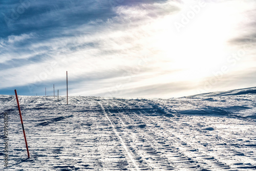 The mountain way for driving of snow mobiles, marked by red orange sticks, Scandinavian Mountains, cold sunny winter day, typical look for subarctic nature