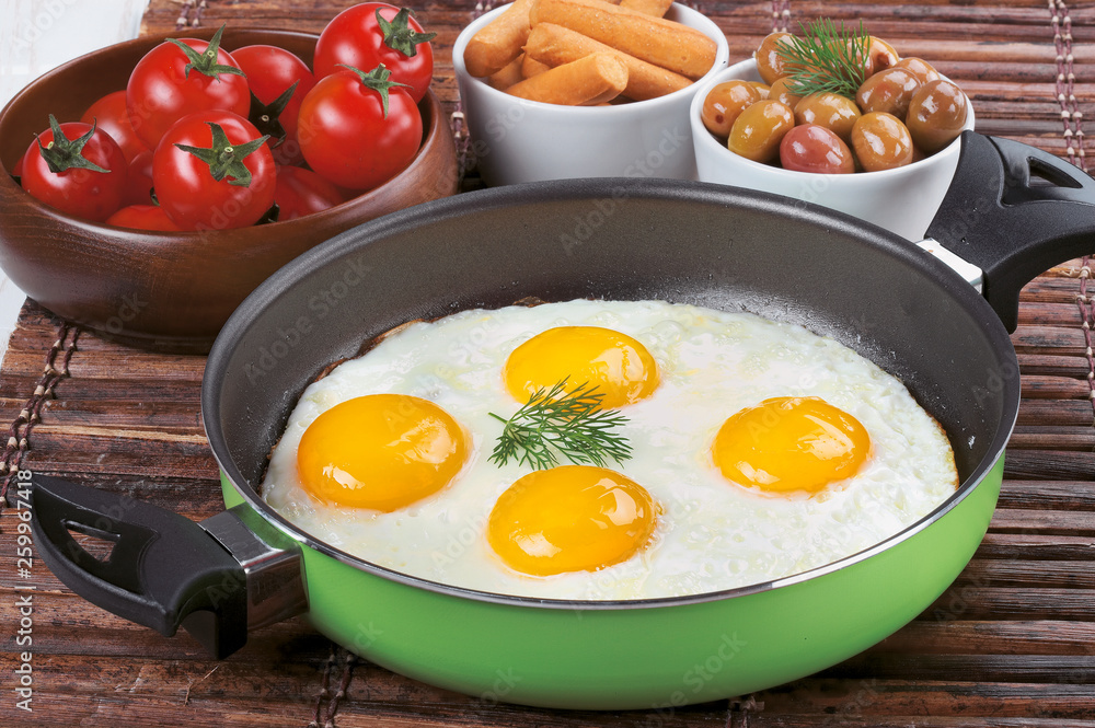 Pan of fried eggs, with cherry-tomatoes and parsley on a wooden table surface. Pan of fried eggs, with cherry-tomatoes and parsley on a wooden table surface.