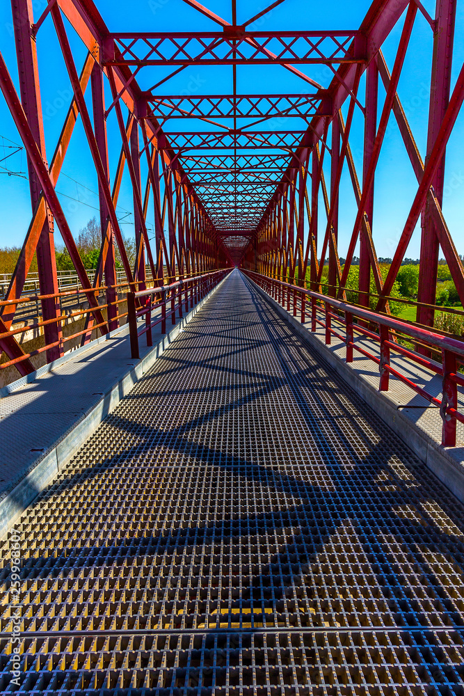 Metallic Red Bridge Over a River Under a Bright Blue Sky Metallic Red Bridge Over a River Under a Bright Blue Sky