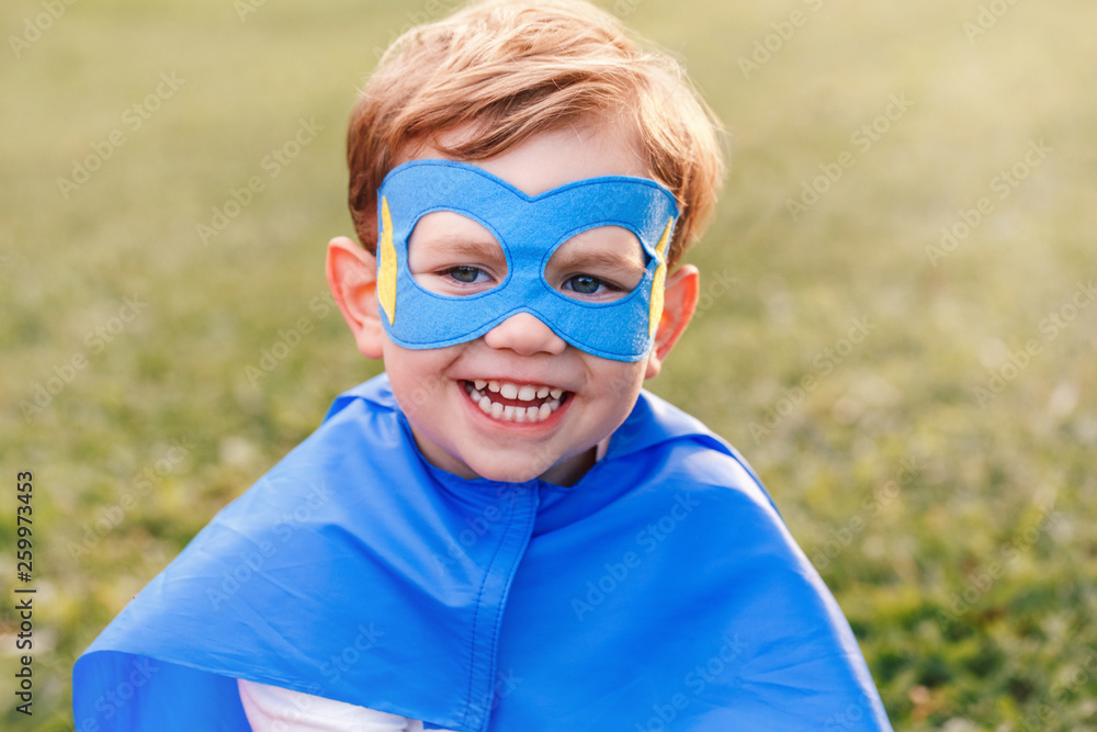 Cute smiling preschool Caucasian child playing superhero in blue costume. Boy kid wearing mask and cape having fun outdoors in park. Happy active childhood. Power and protection concept. Cute smiling preschool Caucasian child playing superhero in blue costume. Boy kid wearing mask and cape having fun outdoors in park. Happy active childhood. Power and protection concept.