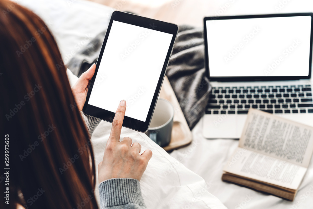 Woman relaxing and using digital tablet computer with white mockup blank screens on the bed at home.woman checking social apps and working..Communication and technology concept Woman relaxing and using digital tablet computer with white mockup blank screens on the bed at home.woman checking social apps and working..Communication and technology concept