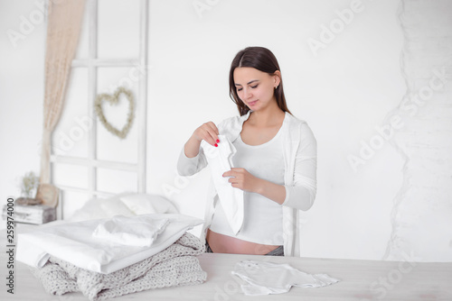 Pregnant girl folds baby clothes in a pile. Women's responsibilities at home. Folding clothes.