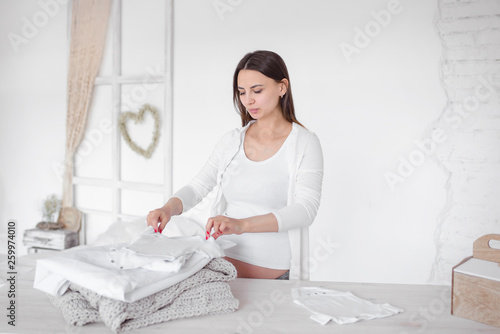 Pregnant girl folds baby clothes in a pile. Women's responsibilities at home. Folding clothes.